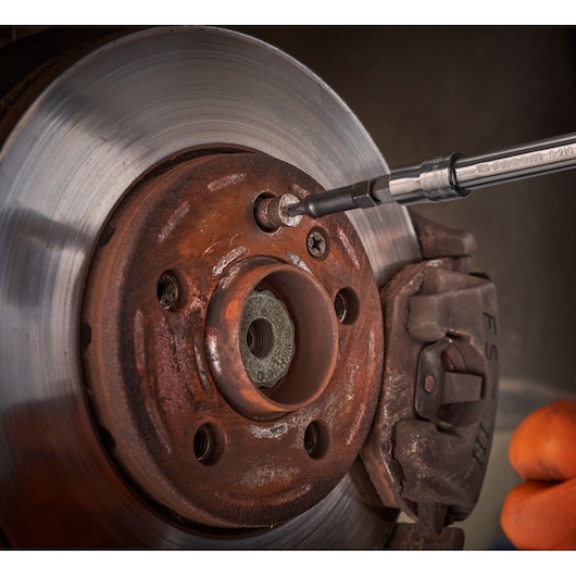 Facom SXE_J7MGRPPB screwdriver in use on rusted car brake disc, close-up with visible tool tip and brake components.