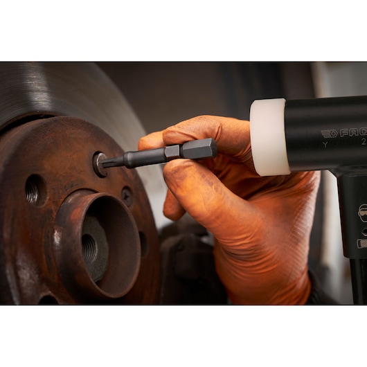 Facom SXE_J7MGRPPB hex bit in use with power tool, close-up of automotive repair, gloved hand.