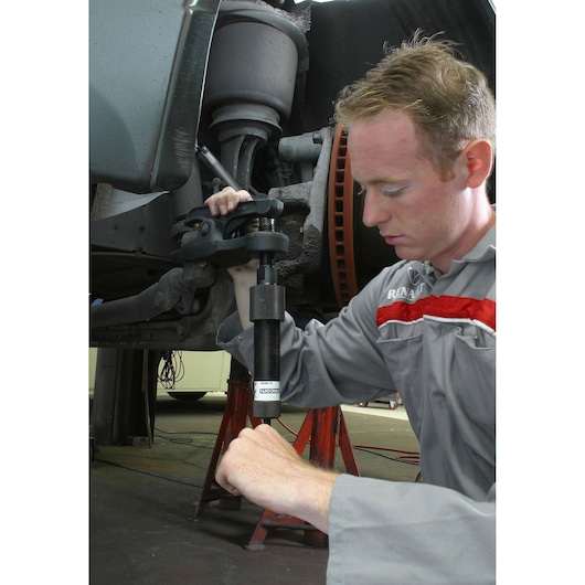 Facom U_18H36 ball joint separator tool used on a car suspension by mechanic in workshop.
