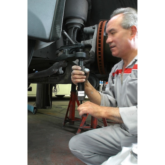 Facom U_18H36 tool used by mechanic for vehicle suspension repair, shown in workshop setting.