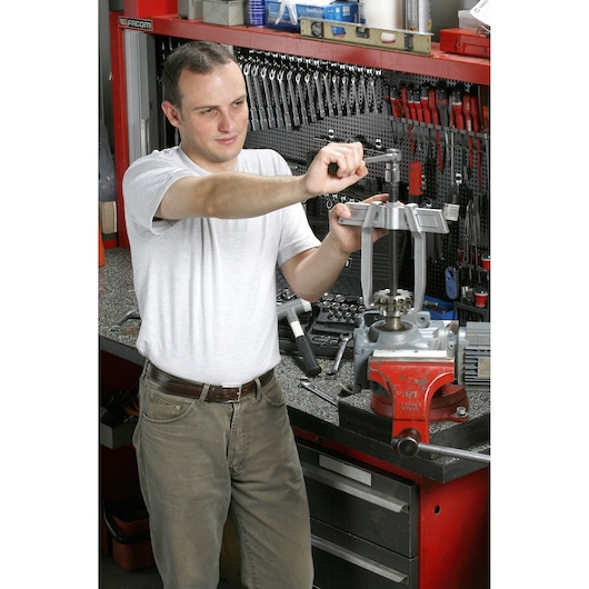 Facom U_232-130 workshop scene with person using tool at workbench with various hand tools on wall.