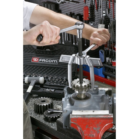 Facom bearing puller in use on gear mounted in vice, hands operating tool. U_232-340, workshop tools background.