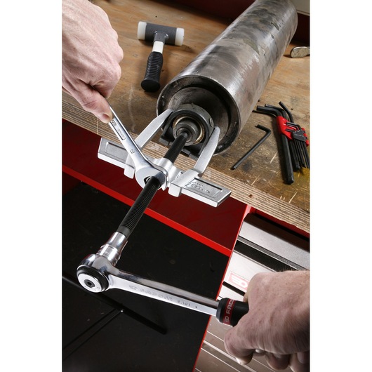 Facom U_232-340 bearing puller in use, removing a bearing from a metal cylinder on a workbench, side angle.