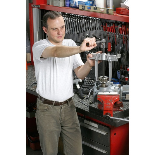 Facom U_232-65 workshop photography showing a person using hand tools at a workbench with a vise and mechanical parts.