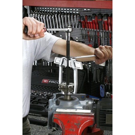Photo of Facom U_232-90 puller tool being used to remove a gear from machinery in a workshop setting.