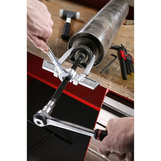 Facom U_232-90 bearing puller used on a metal cylinder, with hand tools visible on workbench.