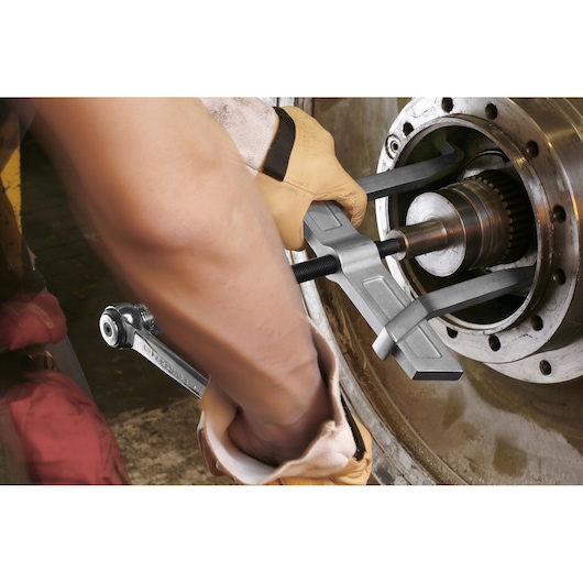 Facom U232J2PB gear puller tool in use on metal machinery, worker wearing gloves.