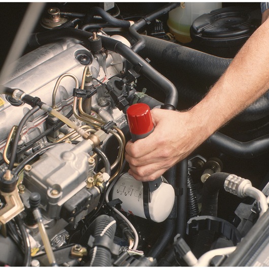 Facom U_46ACL hand tool with red cap used for fluid extraction in a car engine bay, close-up side view.