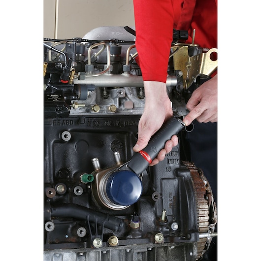 Facom U.48PB filter wrench being used by a mechanic to remove an oil filter from an engine.