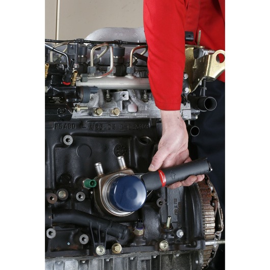 Facom U_48PL oil filter wrench used on engine by person in red uniform, close-up view.