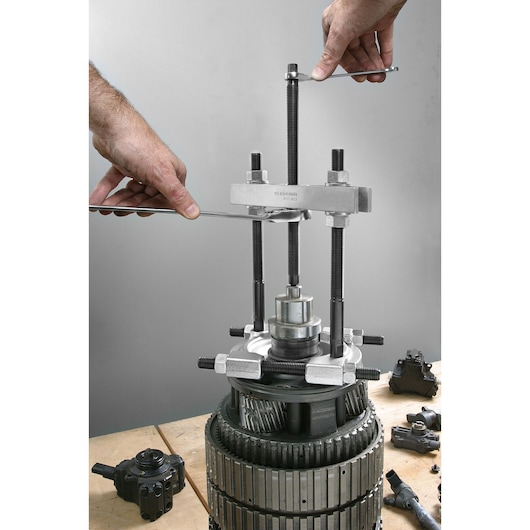 Facom U_53KL2 bearing puller tool in use on a mechanical assembly, close-up view with hands operating the tool.
