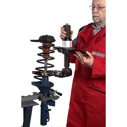 Facom U_89JMA photography of mechanic using spring compressor tool on car strut, side angle.