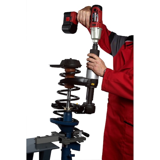 Facom U_89JMA automotive tool in use compressing a car suspension spring, person in red workwear.