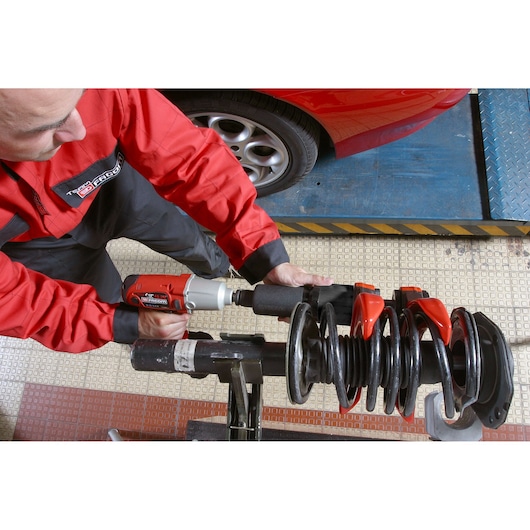 Facom U_89M230 photography of technician using impact wrench on car suspension spring in workshop.