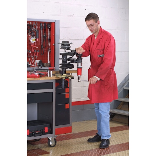 Facom U_89M2 automotive tool on workbench with technician in red coat using compression device.