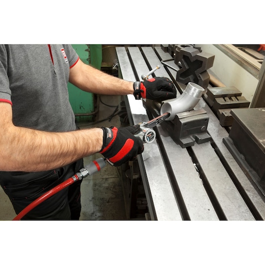 Facom V_402F pneumatic tool used by person wearing gloves to work on metal pipe in workshop.