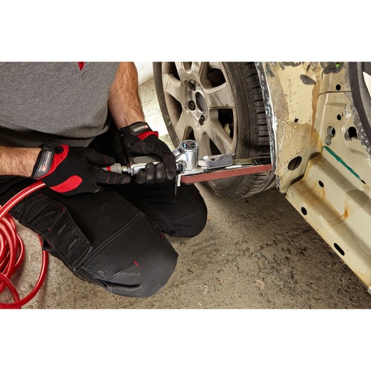 Facom V_403F belt sander used on car body panel, worker wearing black and red gloves.