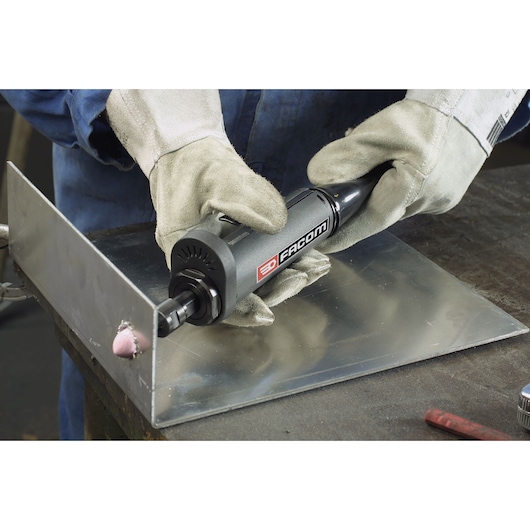 Facom V_445F straight die grinder in use on a metal sheet, operated by gloved hands.