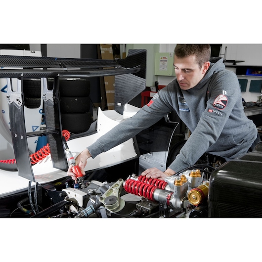 Facom VR_J154 photo showing a mechanic using a Facom tool on a race car suspension in a workshop.