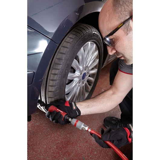 Photo of Facom VR_R227 pneumatic tool used on a car wheel by a mechanic wearing gloves.