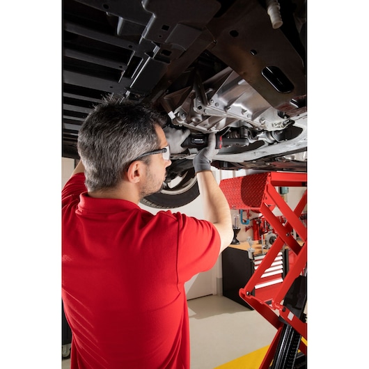 Facom VR_SJ3500PB mechanic in red shirt working under car on red lift in workshop.