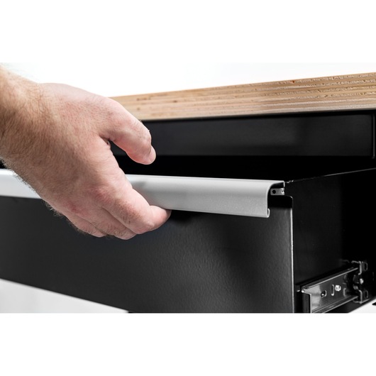 Photo of a hand opening a Facom WB2.1500DRAW black metal drawer under a wooden workbench, close-up angle.
